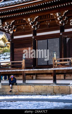 Donna giapponese mascherata seduta su una piattaforma coperta di neve nell'antico complesso sacro del tempio buddista Kiyomizudera a Kyoto, in Giappone Foto Stock