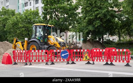 Kiev, Ucraina, 5 giugno 2024. Riparazione stradale su un tratto chiuso con barriere con alberi sullo sfondo. JCB Foto Stock