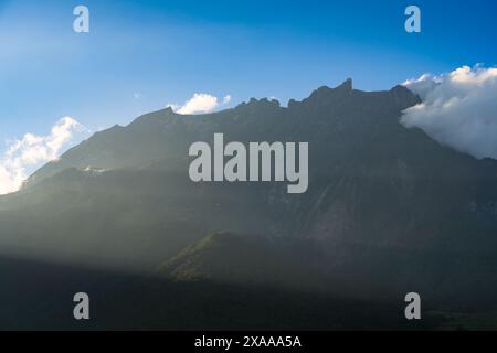 Montagna avvolta da nuvole ed erba sotto il cielo blu Foto Stock