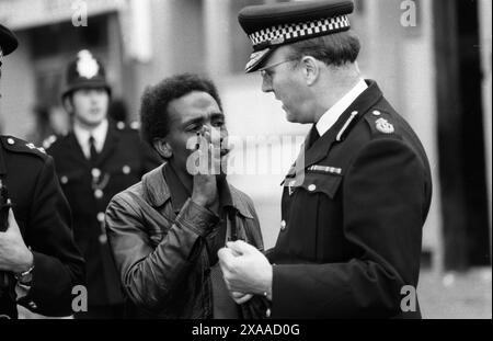 La rivolta del carnevale di Notting Hill agosto festivi lunedì 1976. Un membro anziano della comunità nera dei Caraibi britannici sussurra, trasmette informazioni a un agente di polizia. Notting Hill, Londra, Inghilterra 30 agosto. 1970 UK HOMER SYKES Foto Stock