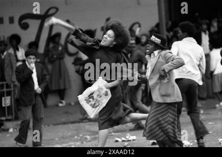 Tumulti di Carnevale di Notting Hill 1976. La polizia viene attaccata prevalentemente dalla comunità nera; una ragazzina lancia un missile nella linea di polizia. Notting Hill, Londra, Inghilterra 30 agosto. 1970 UK HOMER SYKES Foto Stock