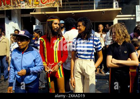 Giovane maschio bianco Rastafarian. L'uomo rastafariano in pantaloncini rossi spogliati e top è conosciuto come Weasel, la ragazza con lui è Anne-Marie Ruddock, che doveva diventare la cantante principale con una band ska reggae degli anni '1980 chiamata Amazulu. Notting Hill, Londra, Inghilterra 27 agosto 1979. 1970 UK HOMER SYKES Foto Stock