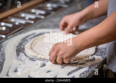 L'impasto per la pizza viene arrotolato e impastato. Cuocere le mani impastando l'impasto e spolverando un pezzo di impasto con farina di grano bianco. Impastare l'impasto per la pizza Foto Stock