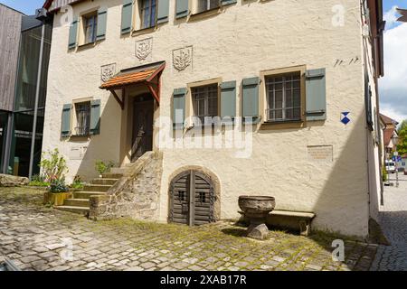 Feuchtwangen, Germania - 6 giugno 2023: Un edificio bianco con porte in legno e gradini in pietra, situato in un cortile acciottolato in Germania. Foto Stock