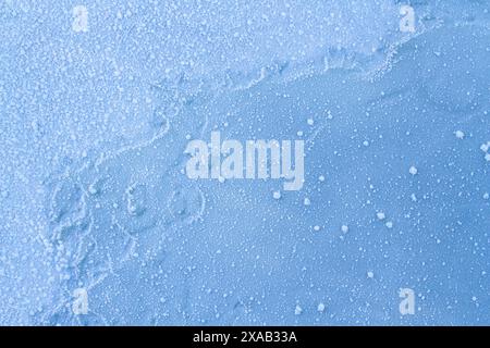 Primo piano foto dettagliate della neve e delle goccioline d'acqua ghiacciate che si trovano sopra un foglio di ghiaccio blu congelato. Foto Stock