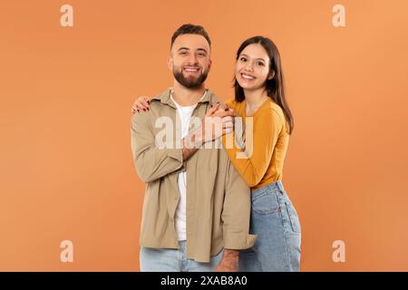 Coppia sorridente in posa su sfondo arancione con abbigliamento casual Foto Stock