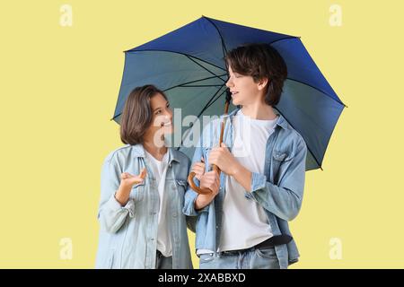 Giovane coppia con ombrello su sfondo giallo Foto Stock