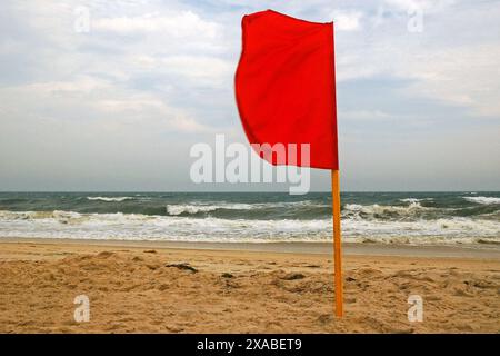 Una bandiera rossa è piantata nella sabbia, vietando il nuoto a causa delle acque scoscese Foto Stock