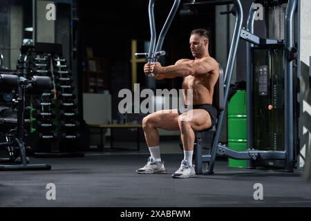 Forte atleta caucasico seduto, allenamento in macchina crossover in palestra. Vista laterale di un atleta sano che esegue pull-down, sollevamento di piastre metalliche della macchina crossover dei cavi, spazio di copia. Concetto di CrossFit. Foto Stock