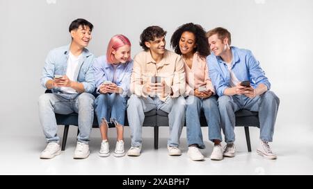 Gruppo diversificato di giovani adulti seduti sul divano, utilizzando smartphone Foto Stock
