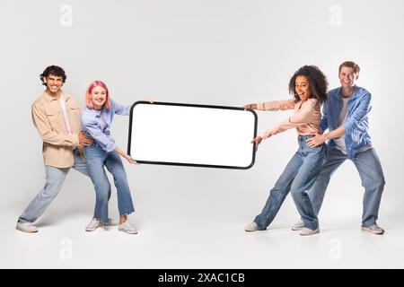 Quattro giovani adulti, due donne e due uomini, stanno tenendo in mano un grande smartphone con schermo vuoto davanti a uno sfondo bianco. Foto Stock