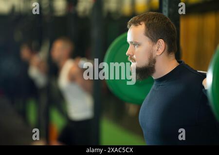 Uomo barbuto che fa esercizi con il barbell durante l'allenamento di gruppo Foto Stock