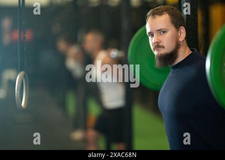 Uomo barbuto che fa esercizi con il barbell durante l'allenamento di gruppo Foto Stock