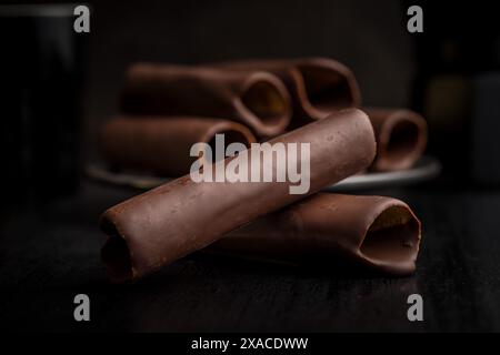 Un bicchierino ravvicinato di cialde ricoperte di cioccolato stese su un tavolo scuro. I wafer sono disposti in un mucchio. L'immagine viene messa a fuoco sulla trama e sui dettagli o Foto Stock