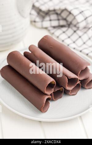 Una foto ravvicinata di wafer ricoperti di cioccolato impilati su un piatto bianco. I rotoli di wafer hanno un interno marrone chiaro visibile attraverso il canale Foto Stock