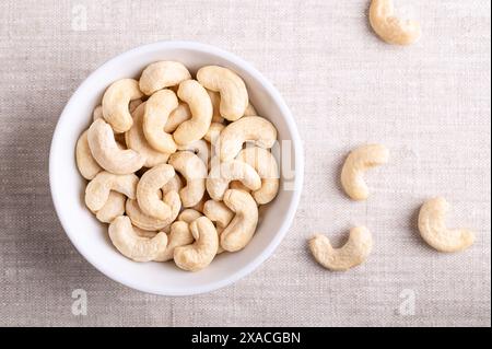 Anacardi, anacardi crudi in una ciotola bianca su tessuto di lino. Semi di frutti sgusciati di anacardi Anacardium occidentale. Foto Stock