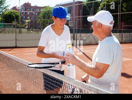 Nonno e nipote che parlano sul campo a giocare a tennis Foto Stock