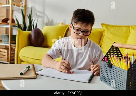 Un ragazzo con la sindrome di Down seduto a un tavolo, concentrato a scrivere su un quaderno. Foto Stock