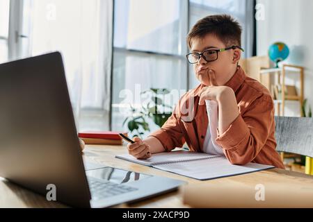 Bambino con sindrome di Down con occhiali studiati sul laptop alla scrivania. Foto Stock