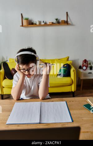 Ragazzo con sindrome di Down che indossa le cuffie, scrivendo in un notebook a casa. Foto Stock