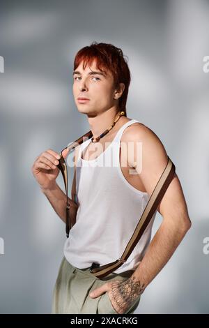 Un giovane uomo elegante con i capelli rossi che si mette in posa con una canotta bianca su uno sfondo grigio studio. Foto Stock