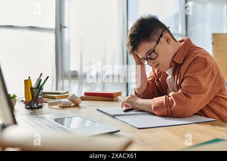 Il bambino con la sindrome di Down siede alla scrivania, utilizzando un computer portatile e un notebook. Foto Stock