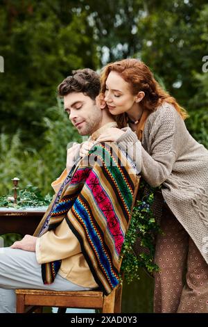 Un uomo e una donna in abiti boho seduti a un tavolo in un parco verde, godendosi un appuntamento romantico. Foto Stock