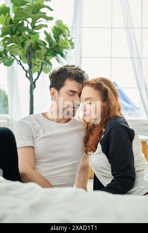 Un uomo e una donna sono seduti a stretto contatto su un letto confortevole, godendosi la compagnia reciproca Foto Stock