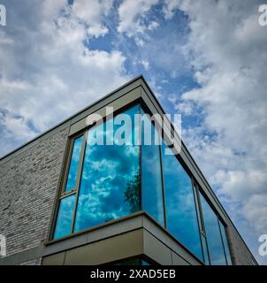 angolo di un edificio moderno con finestre verdi che riflettono le nuvole nel cielo Foto Stock