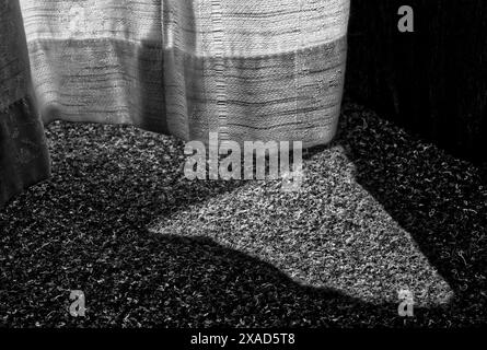 Dettagli del tessuto della tenda e un tappeto in feltro con un triangolo di luce e alcune ombre in bianco e nero Foto Stock