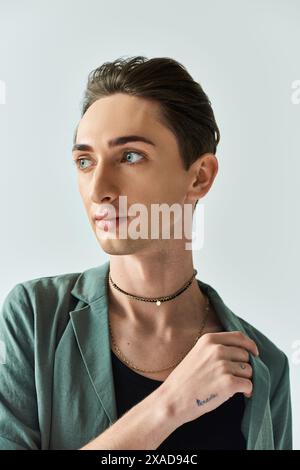 Un giovane queer con una giacca verde vivace mette in posa in studio su uno sfondo grigio. Foto Stock