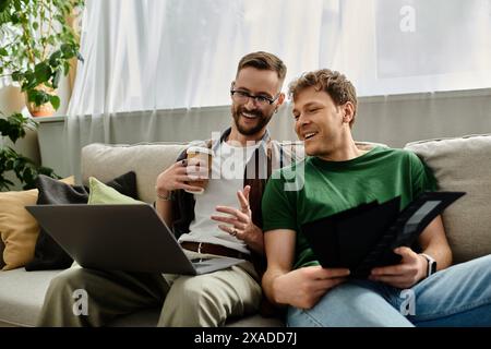 Due uomini innamorati si siedono su un divano, indossando un abbigliamento alla moda su un notebook in un'officina di design. Foto Stock