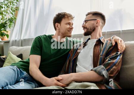 Due uomini alla moda, parte di una coppia gay, si siedono comodamente sul retro di un divano in un elegante laboratorio. Foto Stock