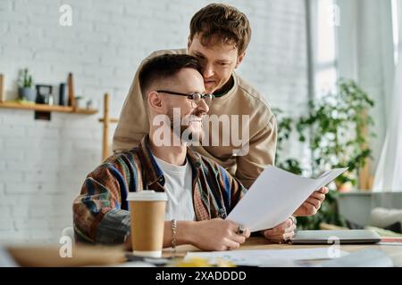 Due uomini seduti a tavola, che esaminano la carta, discutono di disegni per abiti alla moda. Foto Stock