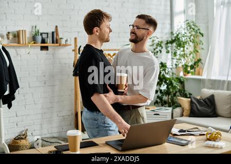 Due designer, una coppia gay, stanno di fronte a un notebook, collaborando su abbigliamento alla moda nel loro laboratorio. Foto Stock