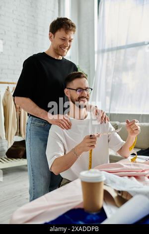 Due uomini stanno accanto a un tavolo, discutendo con passione e progettando abbigliamento alla moda nel loro laboratorio di designer. Foto Stock
