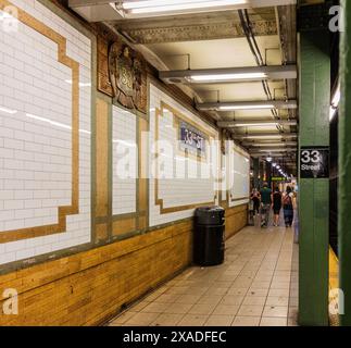 New York City, Stati Uniti - 23 agosto 2017: Nella 33rd Street station della metropolitana di New York City, con targhe di faience (1904) e persone. Foto Stock