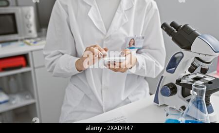 Complessa scienza a portata di mano, giovane e bella scienziata ispanica immersa nell'analisi tecnologica, utilizzando ingegnosamente lo smartphone del Foto Stock
