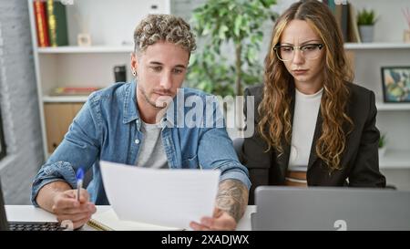 Un uomo e una donna concentrati che collaborano in un ufficio moderno, rivedendo un documento insieme su un notebook. Foto Stock