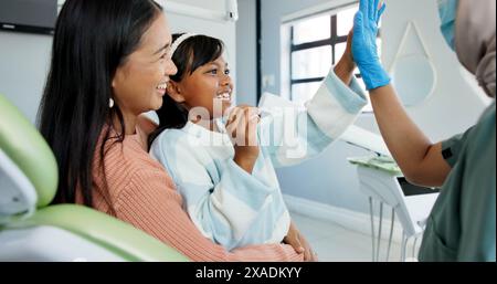 Bambino, dentista pediatrico e alto cinque in checkup, fiducia e buon lavoro per l'igiene orale o denti sani. Ragazza, genitore e supporto in consultazione da Foto Stock