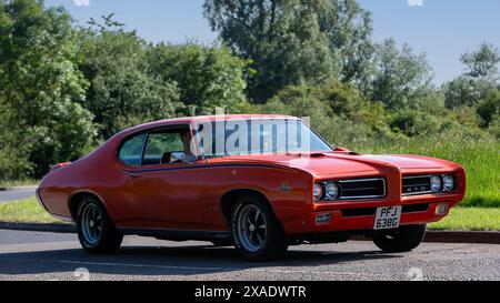 Stony Stratford, Regno Unito - 2 giugno 2024: 1969 Pontiac GTO arancione, classica auto americana, che guida su una strada di campagna britannica Foto Stock