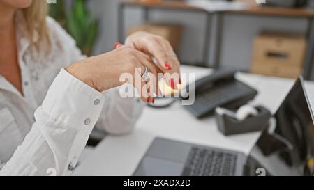 Donna bionda in un ambiente d'ufficio con unghie ben curate che utilizzano una spugna per la pulizia, trasmettendo un messaggio di igiene e multitasking. Foto Stock