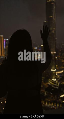 Silhouette di una donna che si affaccia su un paesaggio urbano illuminato di dubai di notte da un osservatorio Foto Stock