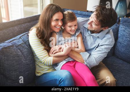 Solletico, ridendo e un bambino con i genitori sul divano di casa rilassarsi con cura, divertimento e amore insieme. Felice, legato e ragazza che gioca con la madre Foto Stock