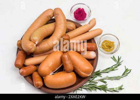 Salsicce di diverse varietà su piatto di ceramica. Senape e rafano in ciotole di vetro, rametti di rosmarino e ciliegie sul tavolo. Sfondo grigio. Piatto Foto Stock