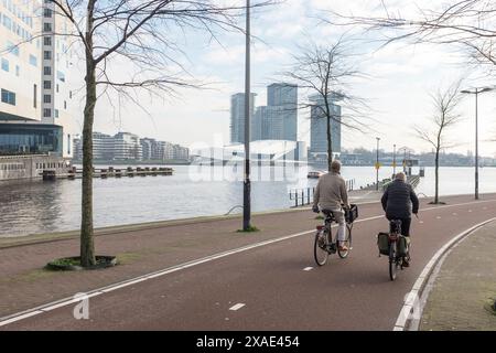 Ciclisti e pedoni viaggiano lungo la Westerdokskade con una vista sul fiume IJ fino ad Amsterdam Nord. Foto Stock