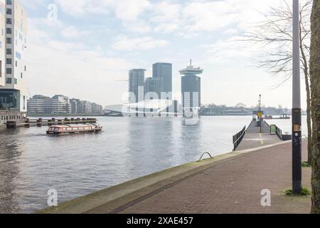 Ciclisti e pedoni viaggiano lungo la Westerdokskade con una vista sul fiume IJ fino ad Amsterdam Nord. Foto Stock