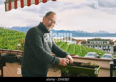 Ritratto di uomo di mezza età piantando piantine sul balcone, piccolo giardino accogliente in appartamento Foto Stock