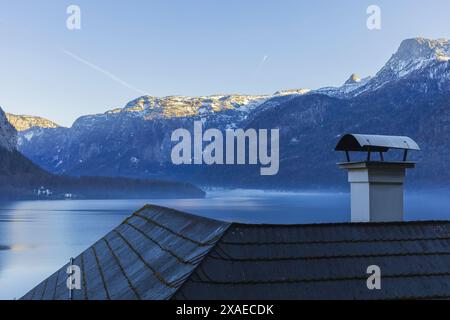 Foto della montagna alpina sopra il tetto della casa con camino al tramonto invernale Foto Stock