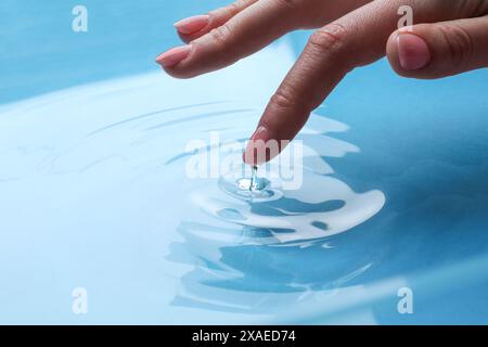 Donna che tocca l'acqua limpida, primo piano. Creare increspature Foto Stock